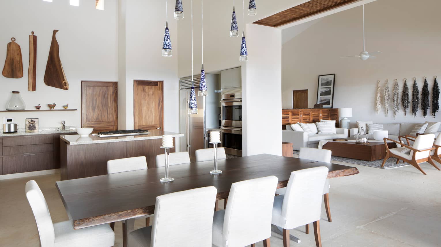 White dining chairs around long wood table under glass lights, modern kitchen