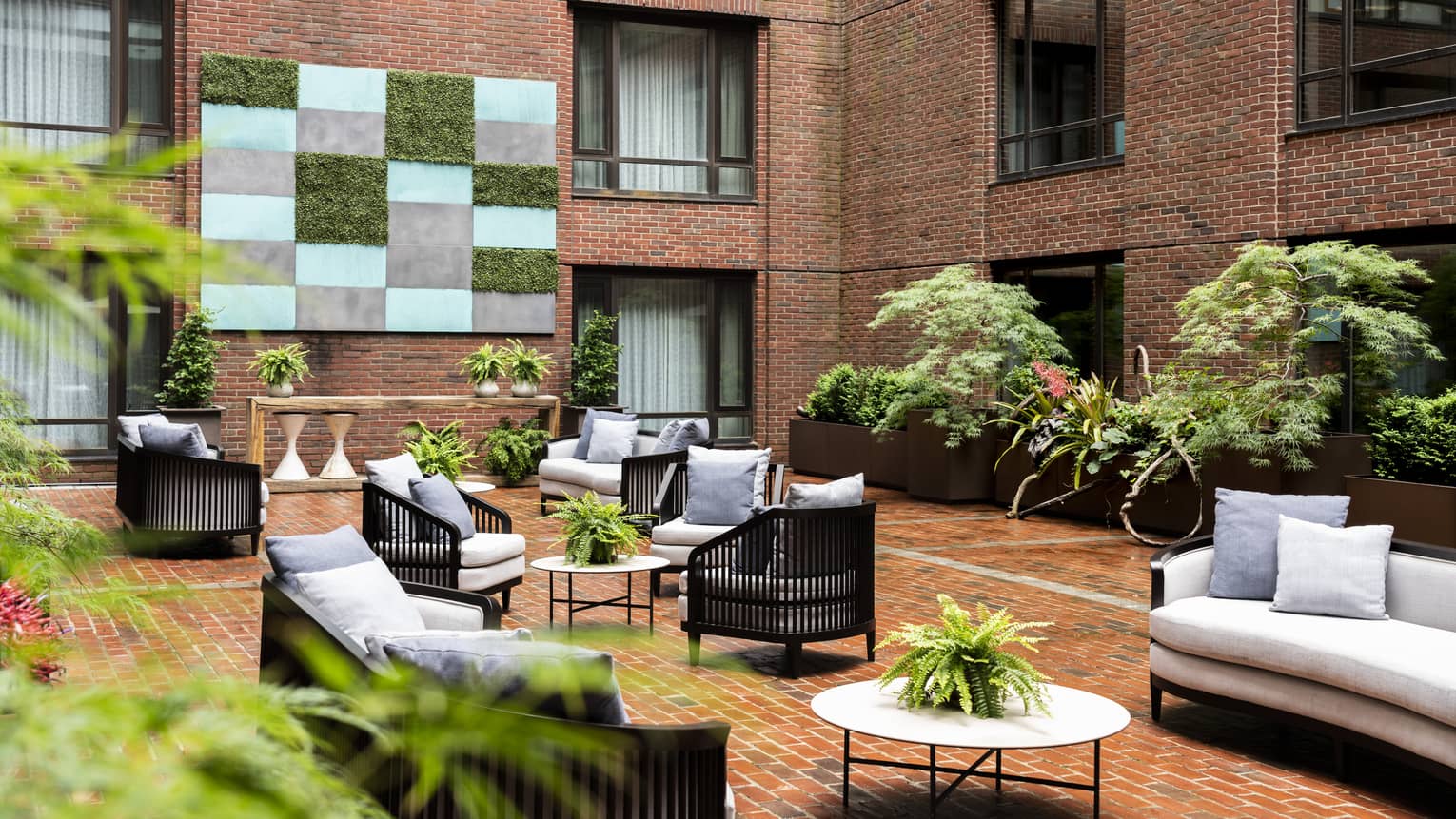 An outdoor seating area with grey sofas and chairs, surrounded by red brick walls.