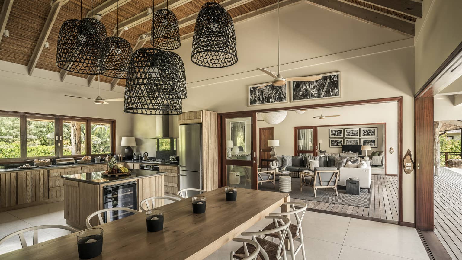 Large basket-like chandeliers hang from gambrel roof over long wood dining table, large kitchen