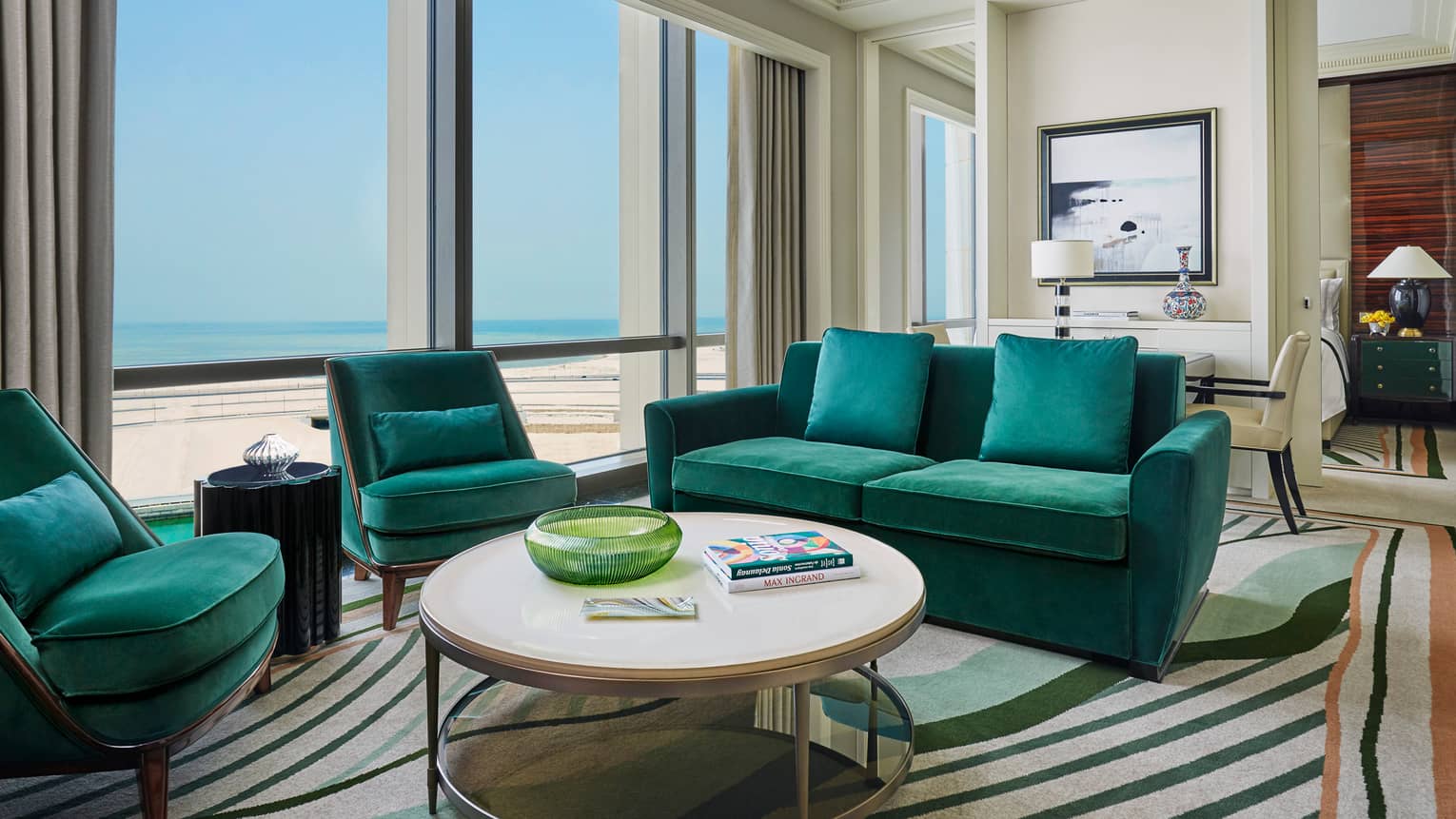Four Seasons Executive Suite with emerald green velvet sofas, armchairs, round coffee table with books, sunny windows