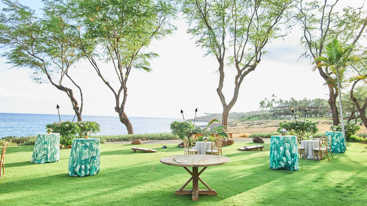 A series of tables with green floral table cloths in a lush green field overlooking a calm sea.