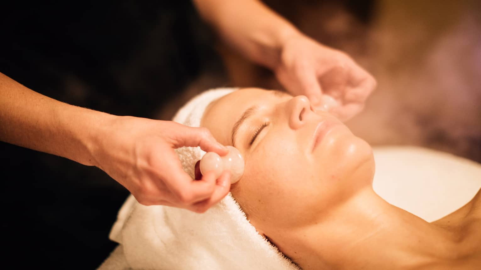 A woman receiving a facial massage with round stones.