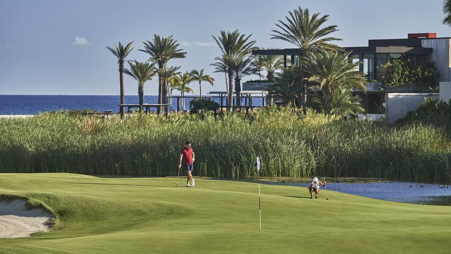 Two golfers enjoy a day on the golf course at four seasons Los Cabos with palm trees and the ocean in the background