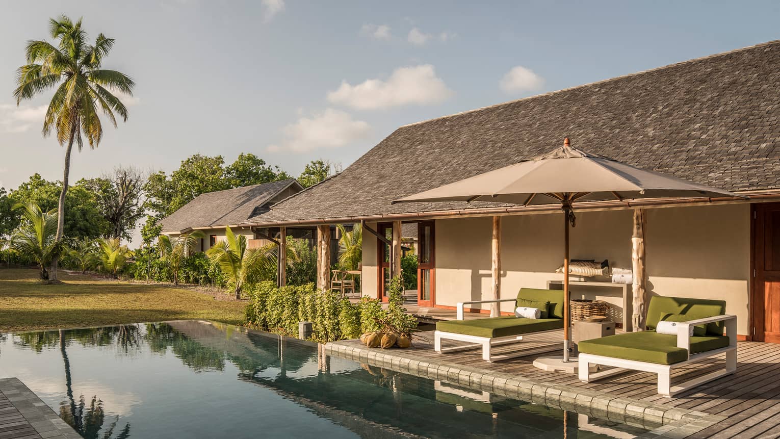 Palm tree reflecting on plunge pool under bungalow small patio with two lounge chairs, umbrella