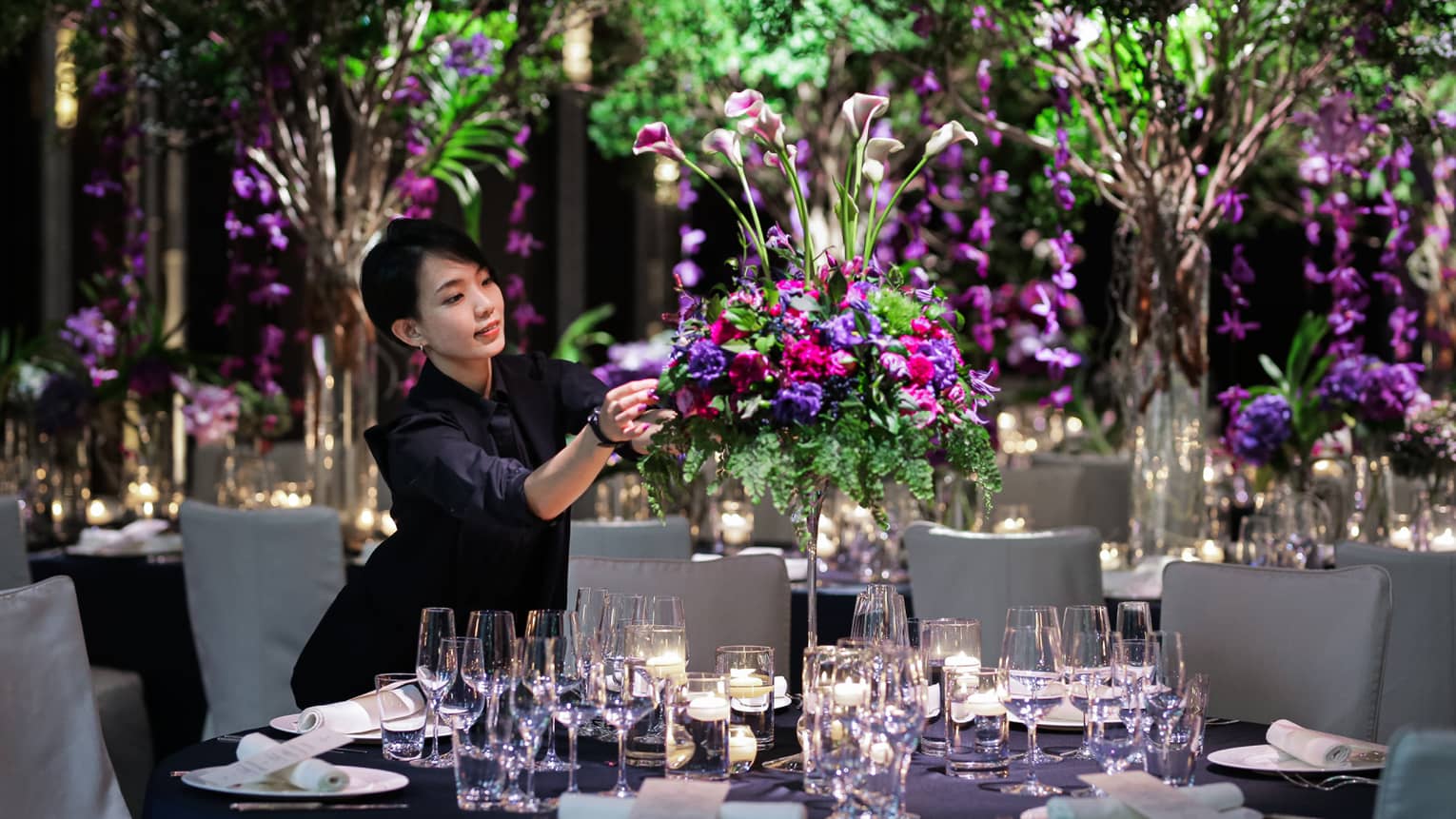 Wedding event staff arranges large floral centrepiece on banquet table