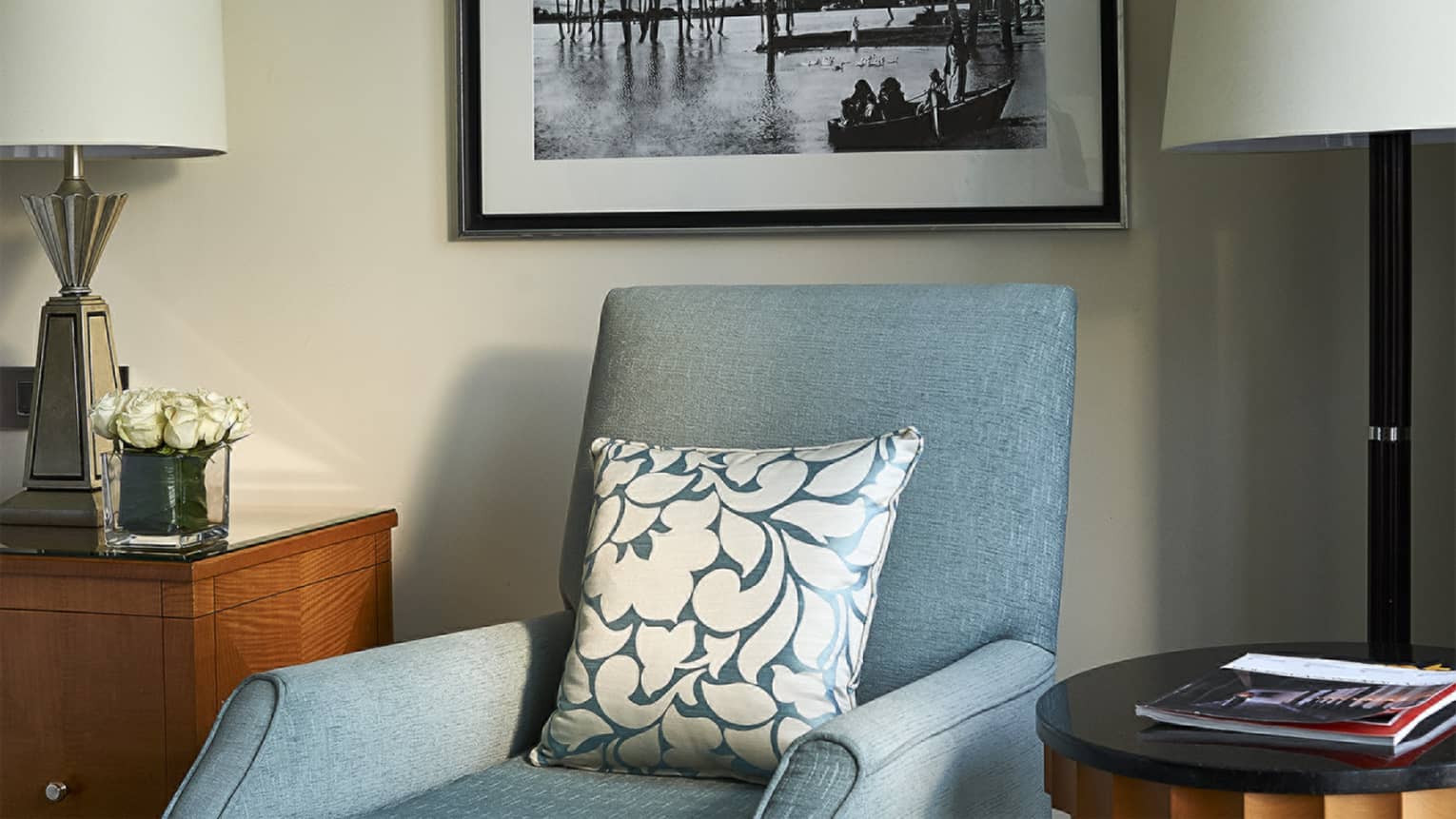 Blue armchair with patterned pillow in guest room next to side table with magazine