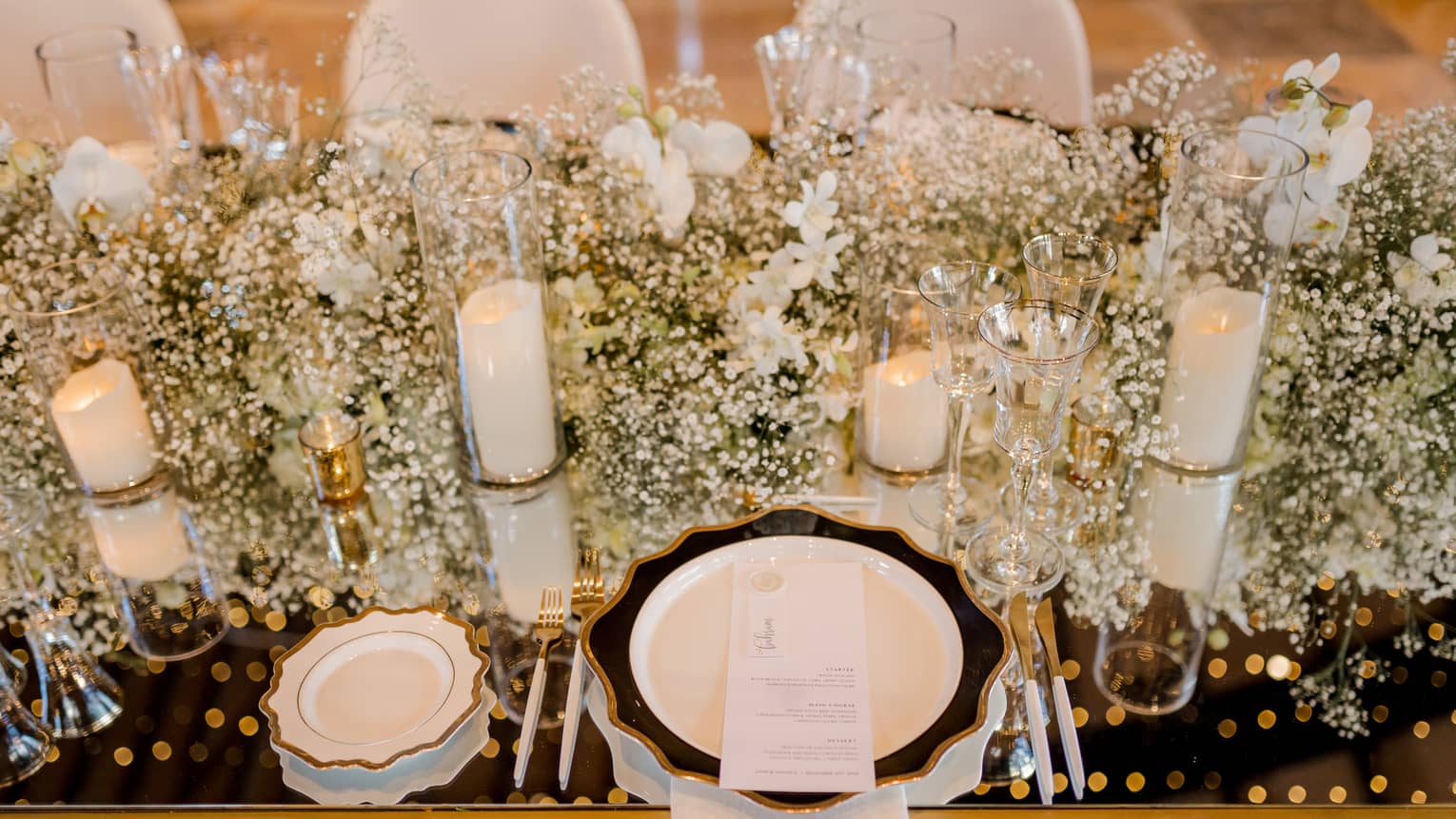 Closeup of table set for wedding reception with white flowers, candles, chair covers and dishes