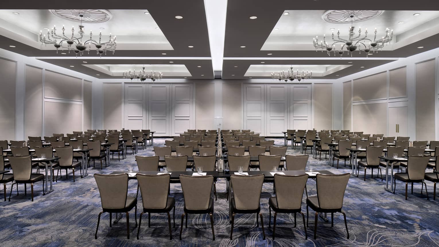 Large ballroom with inset ceilings, recessed lighting, and chandeliers, with several rows of tables and chairs