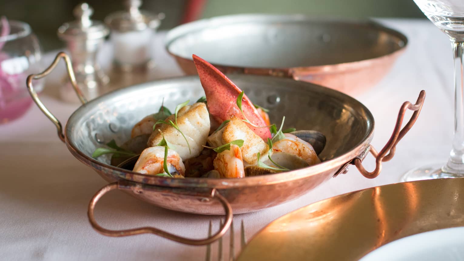 Close-up of copper bowl on table with lobster claw meat, seafood, green herb garnish