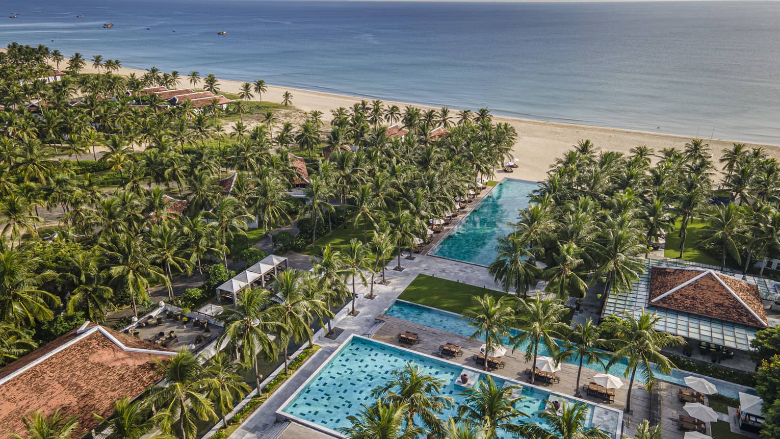 Aerial view of the resort pools with ocean views, palm trees and blue skies