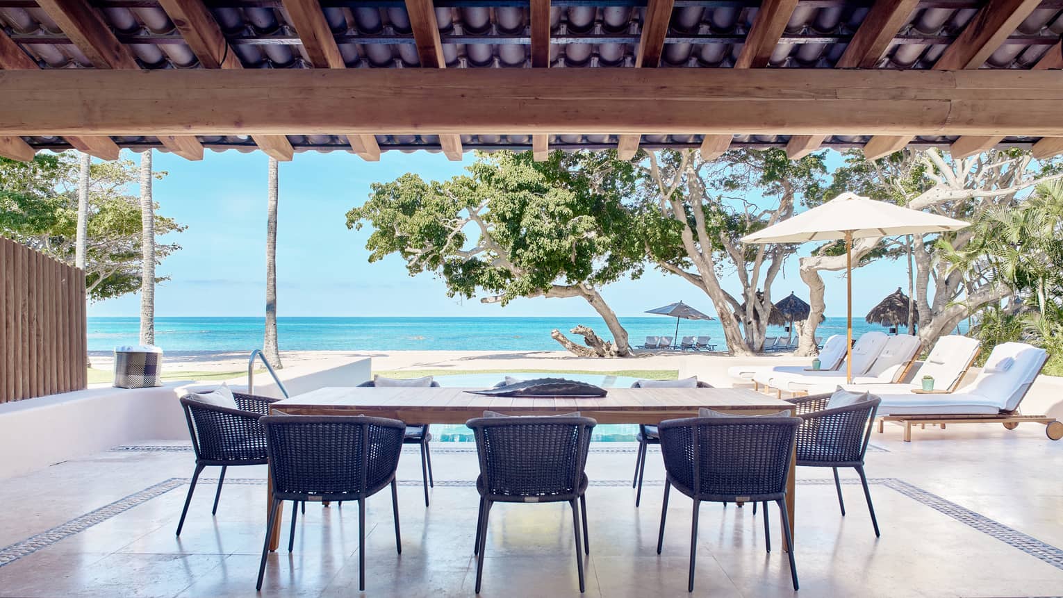 Arena Beach House open-air dining area with rectangular table, eight rattan chairs, portico for shade