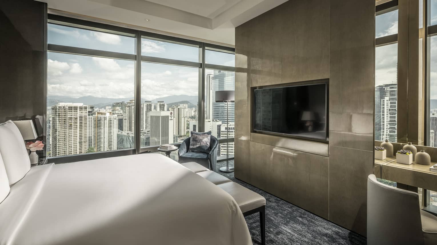 Bed across from desk and modern wood panel wall with TV, by floor-to-ceiling window