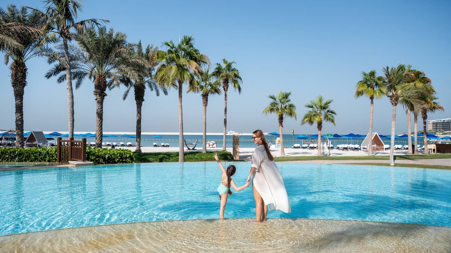 A woman and a little girl hold hands while wading in the outdoor pool overlooking the Arabian Gulf