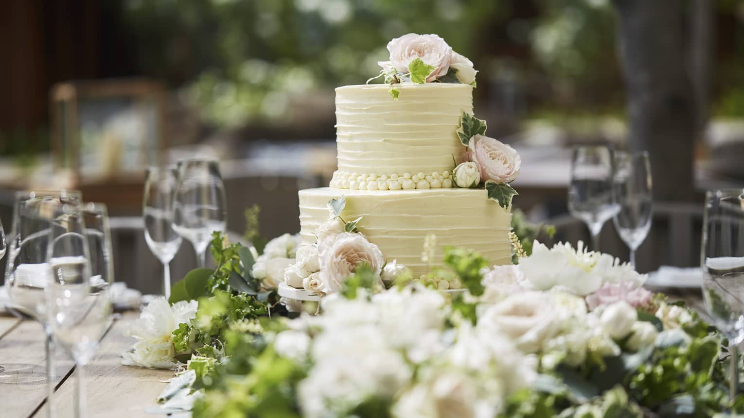 Two-tiered white wedding cake on banquet table with wine glasses, flowers