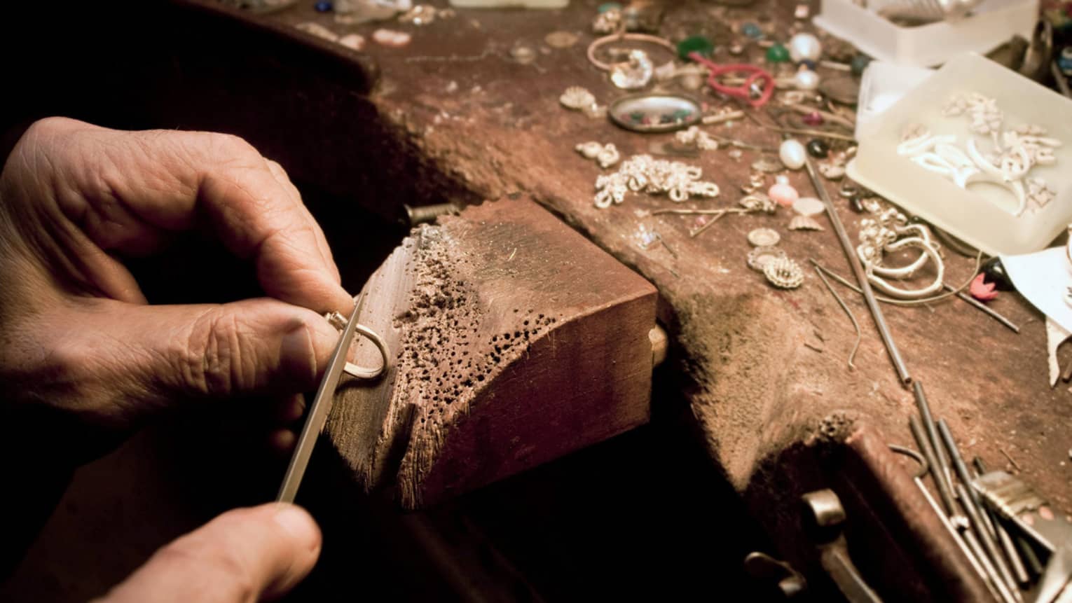 Jeweller's hands using a tool to craft jewellery on a wooden block