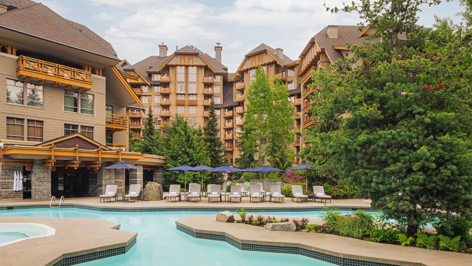 An outdoor pool next to a large hotel building with trees near the pool.