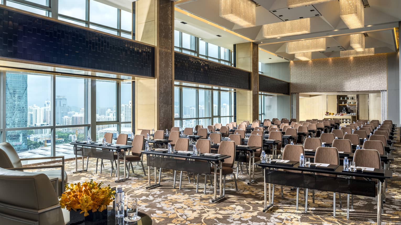 Rows of small meeting tables and chairs in row in large meeting room with loft-like windows, ceiling