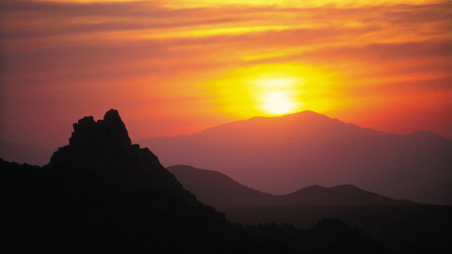 Silhouette of Pinnacle Peak mountain in front of orange sunset