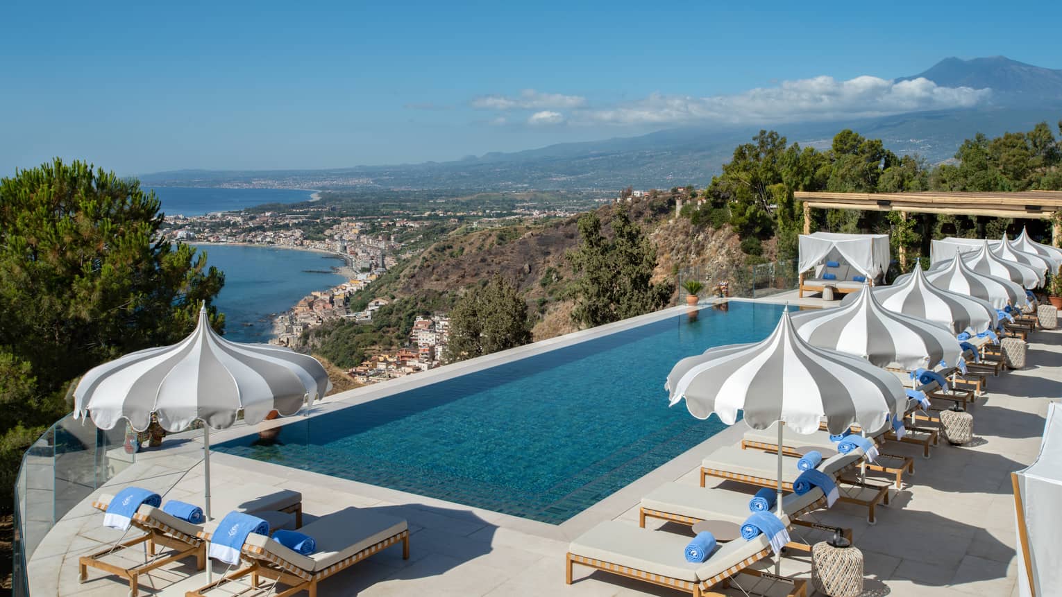 Rectangular pool, lounge chairs and umbrellas overlooking sea and Mount Etna
