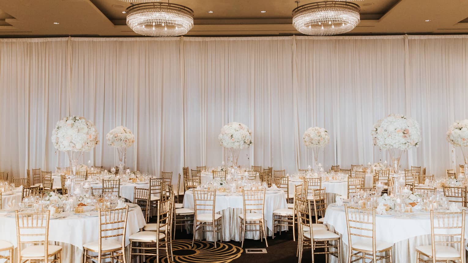 Elegant gold and white banquet dining tables in event room with small round chandeliers