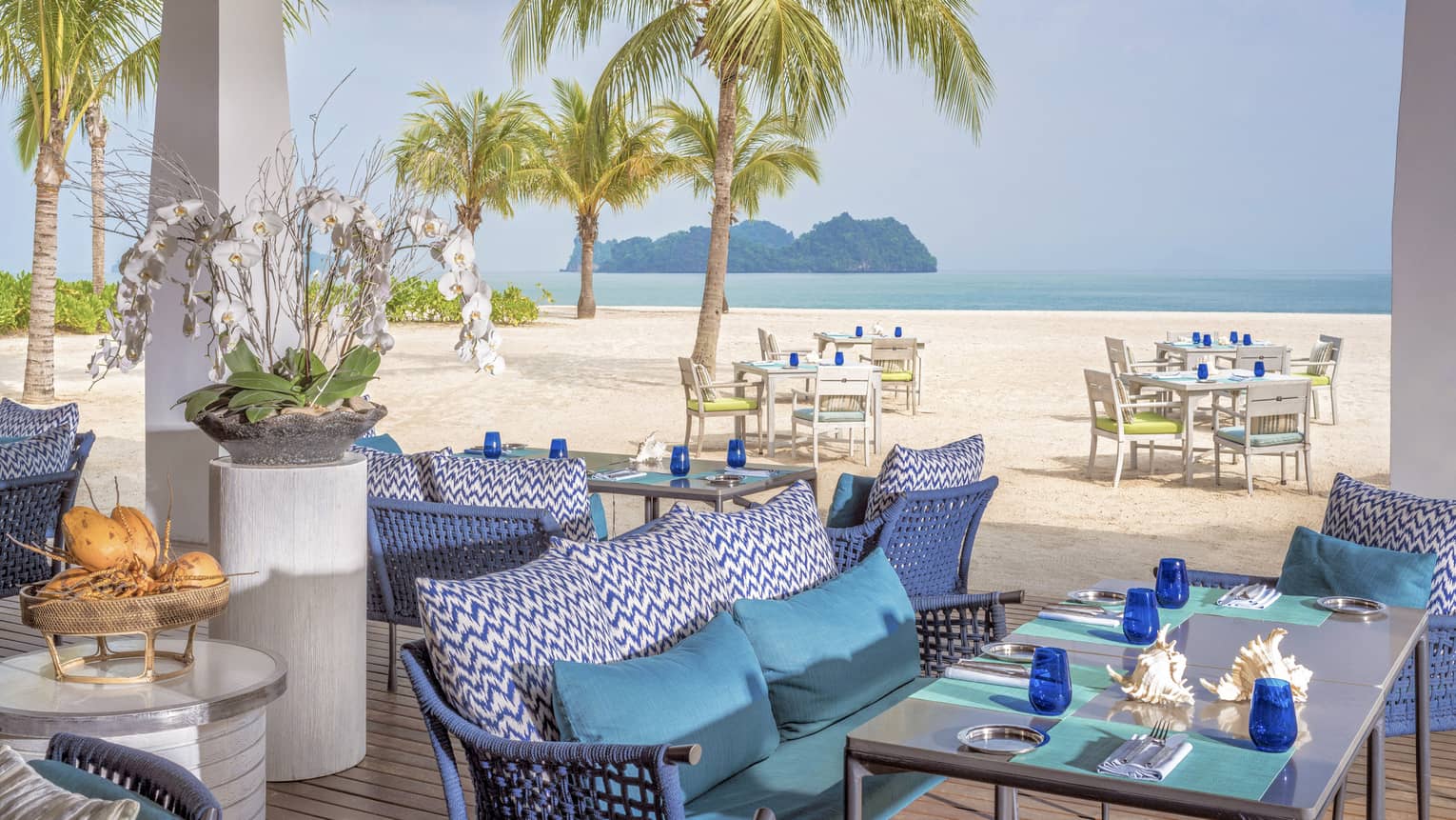 Terrace of ocean-view restaurant, blue cushions on sofa, turquoise place mats and blue glasses on table