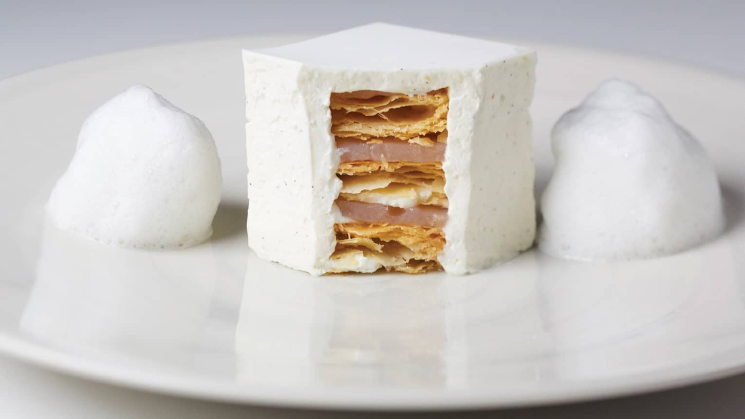 White foam flanks white millefeuille cut open in center, showing layers on white plate