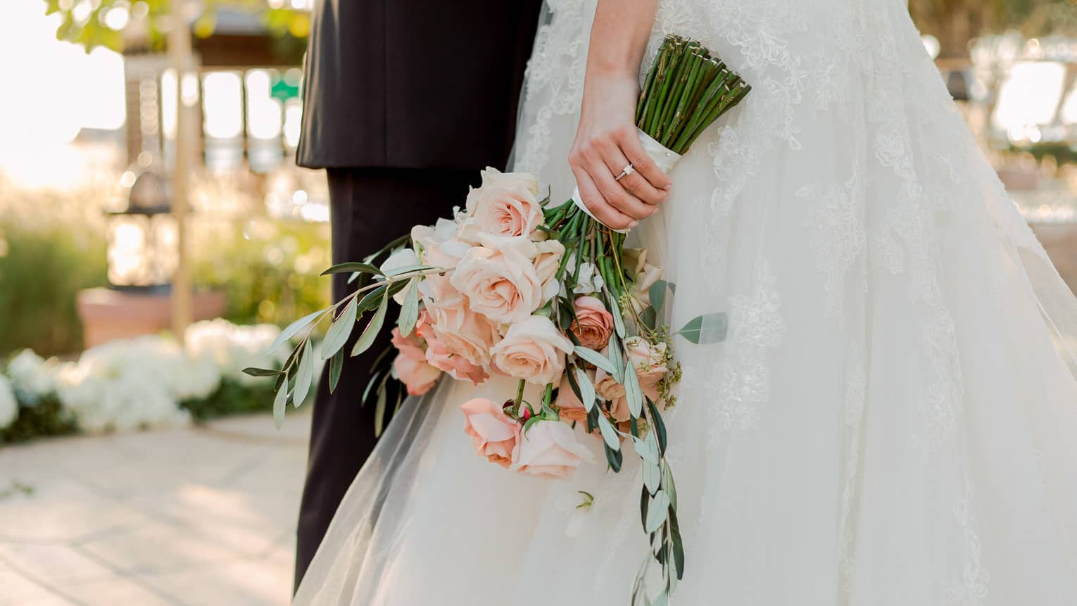 Groom and bride holding wedding floral bouquet of long-stemmed pink roses 