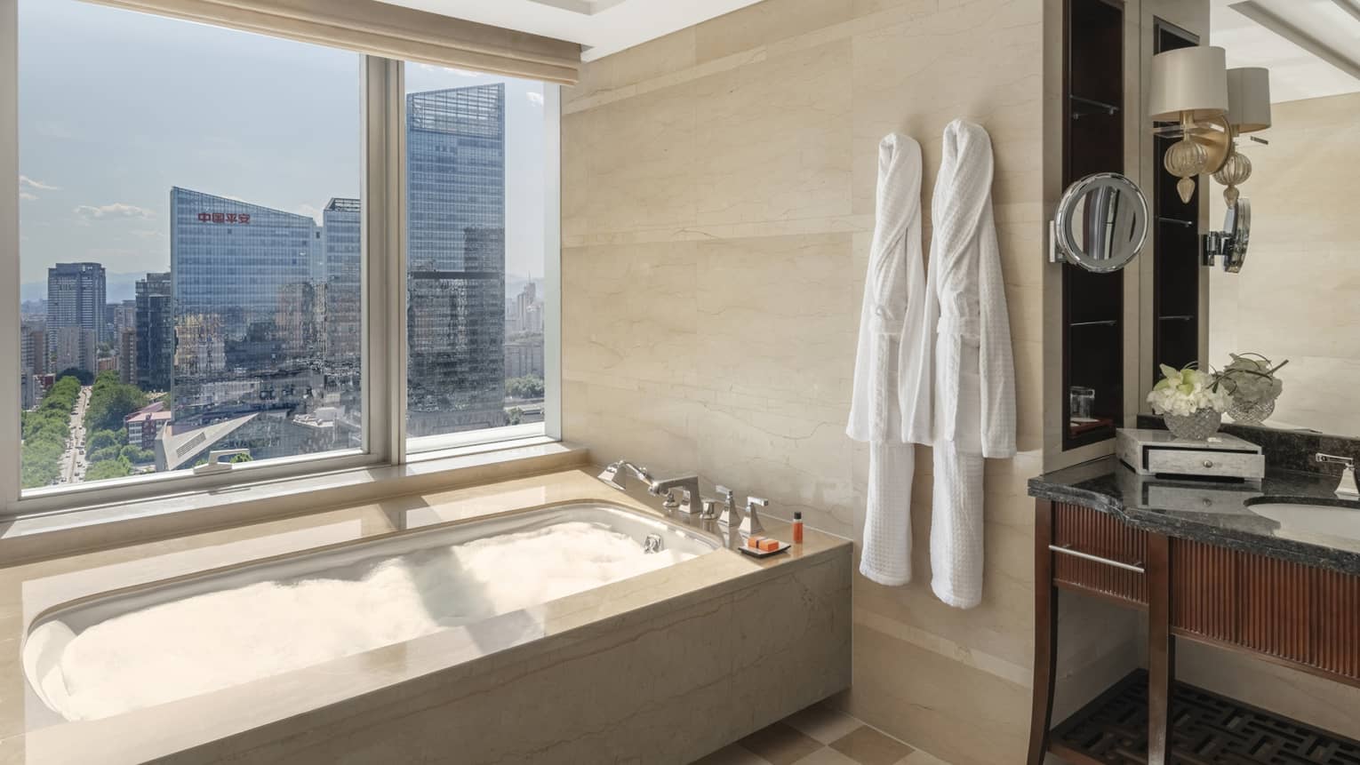 Bathroom with tan and white tile floor, two robes hanging on wall hooks, and a windowside tub