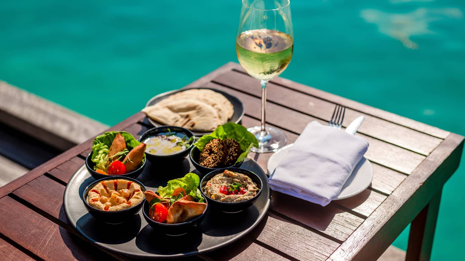 Arabic mezze platter and glass of white wine on poolside table