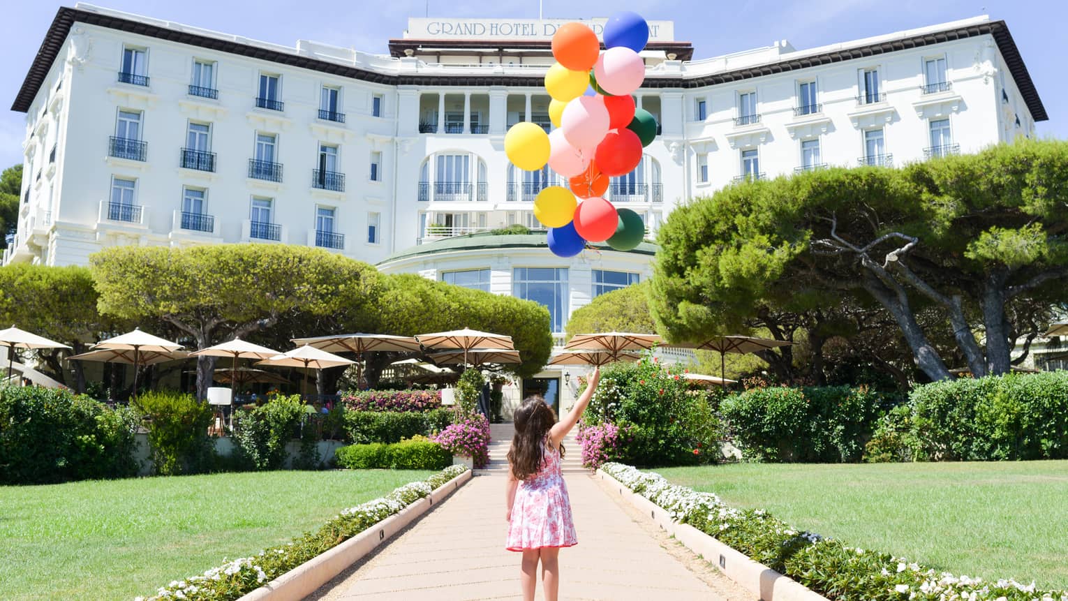 Young girl holds bunch of colourful balloons on brick path leading to hotel