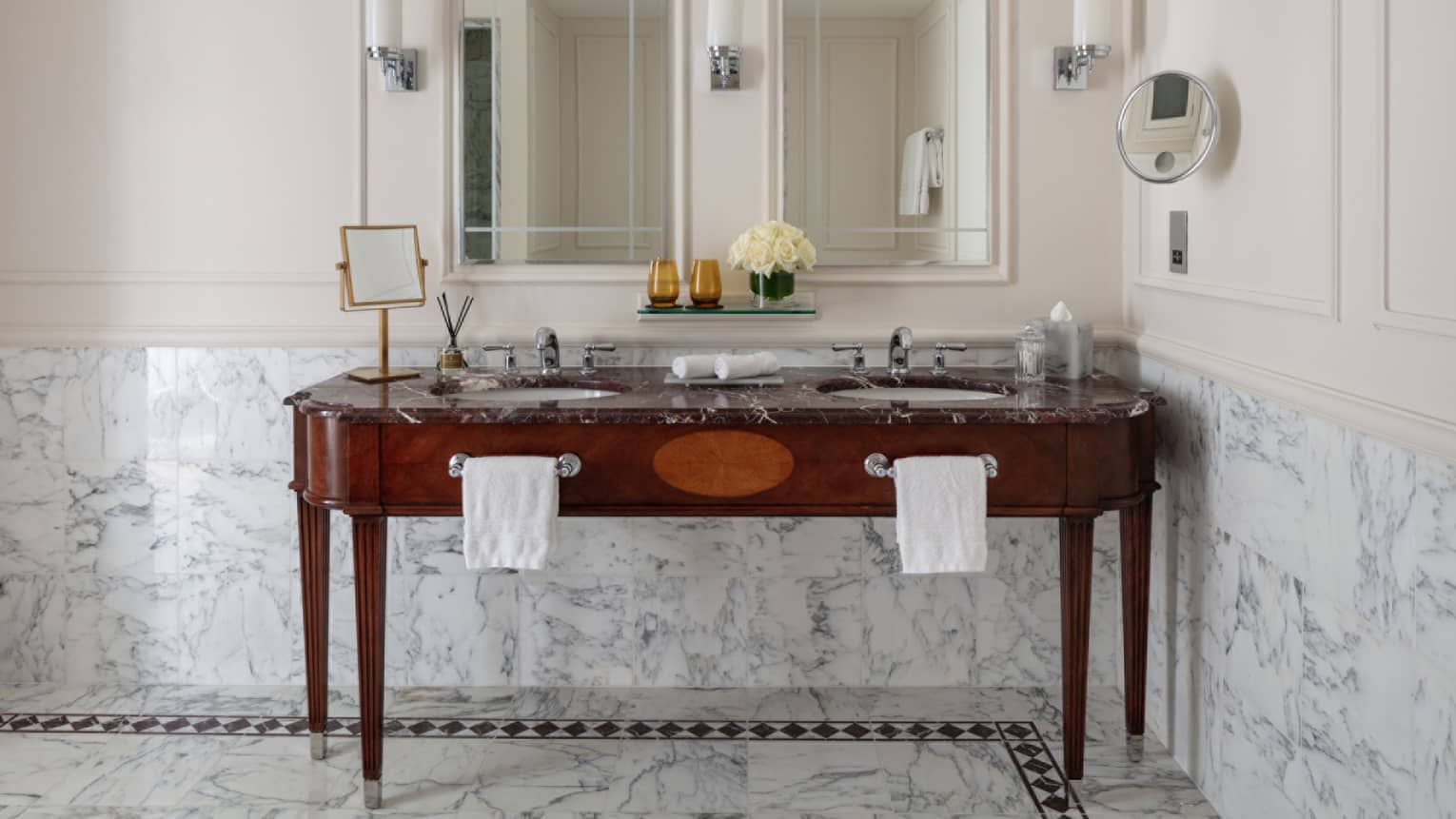 Bathroom with double wooden vanity, double mirror, marble tiles at chair rail, lighted wall sconces