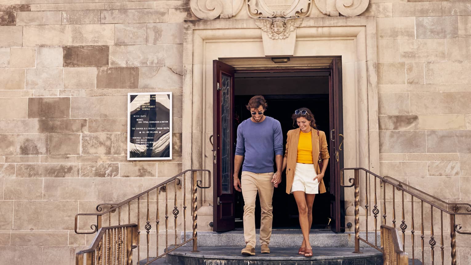 A man and woman walking out of an old stone building.