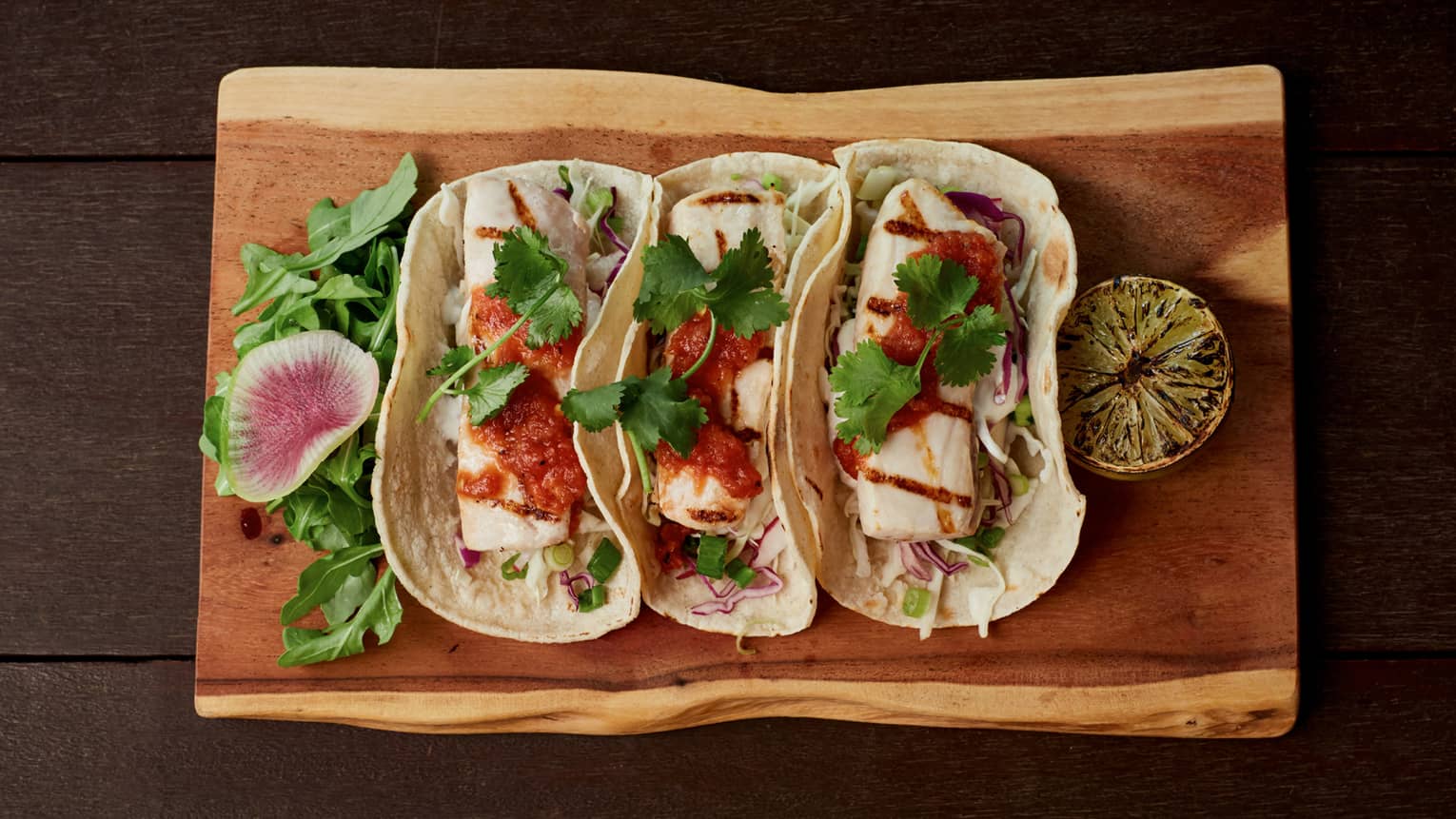 Aerial view of three large fish tacos, sauce on rustic wood platter