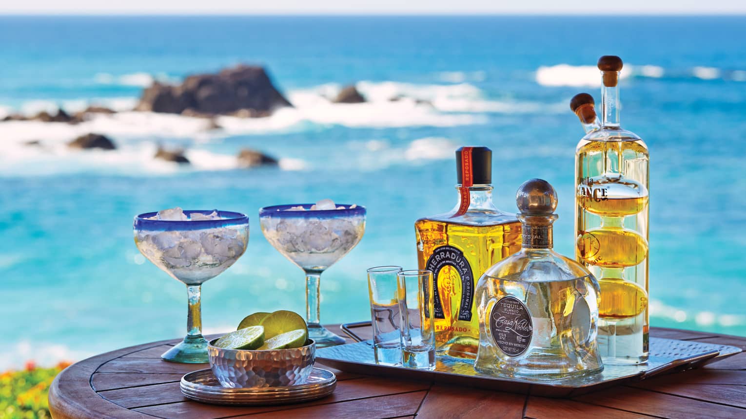 Close-up of Cora Lounge table, tray with tequila bottles, two margarita glasses with ice, bowl of limes