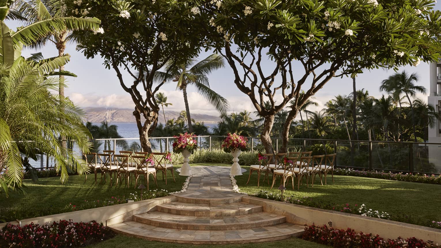 Outdoor wedding with chairs, flowers facing towards ocean and island, surrounded by trees 