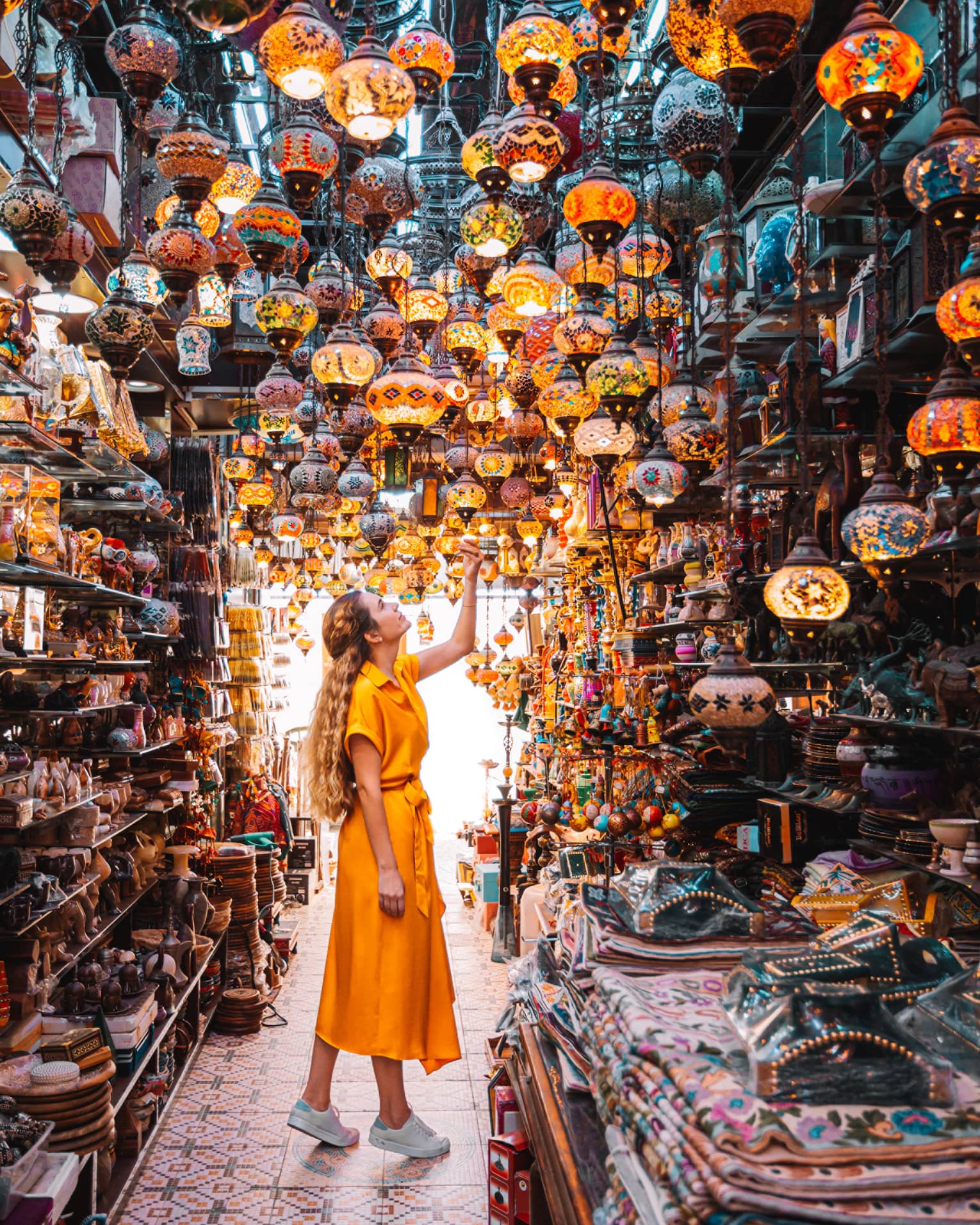 A woman in a yellow dress stands in the centre of a market under a series of bright lamps.