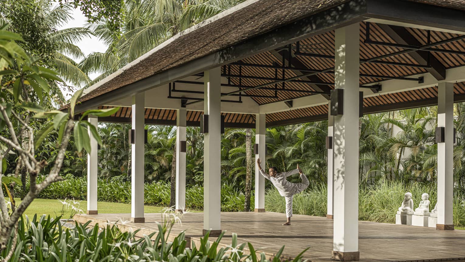 Man does yoga in outdoor yoga pavilion surrounded by palm trees