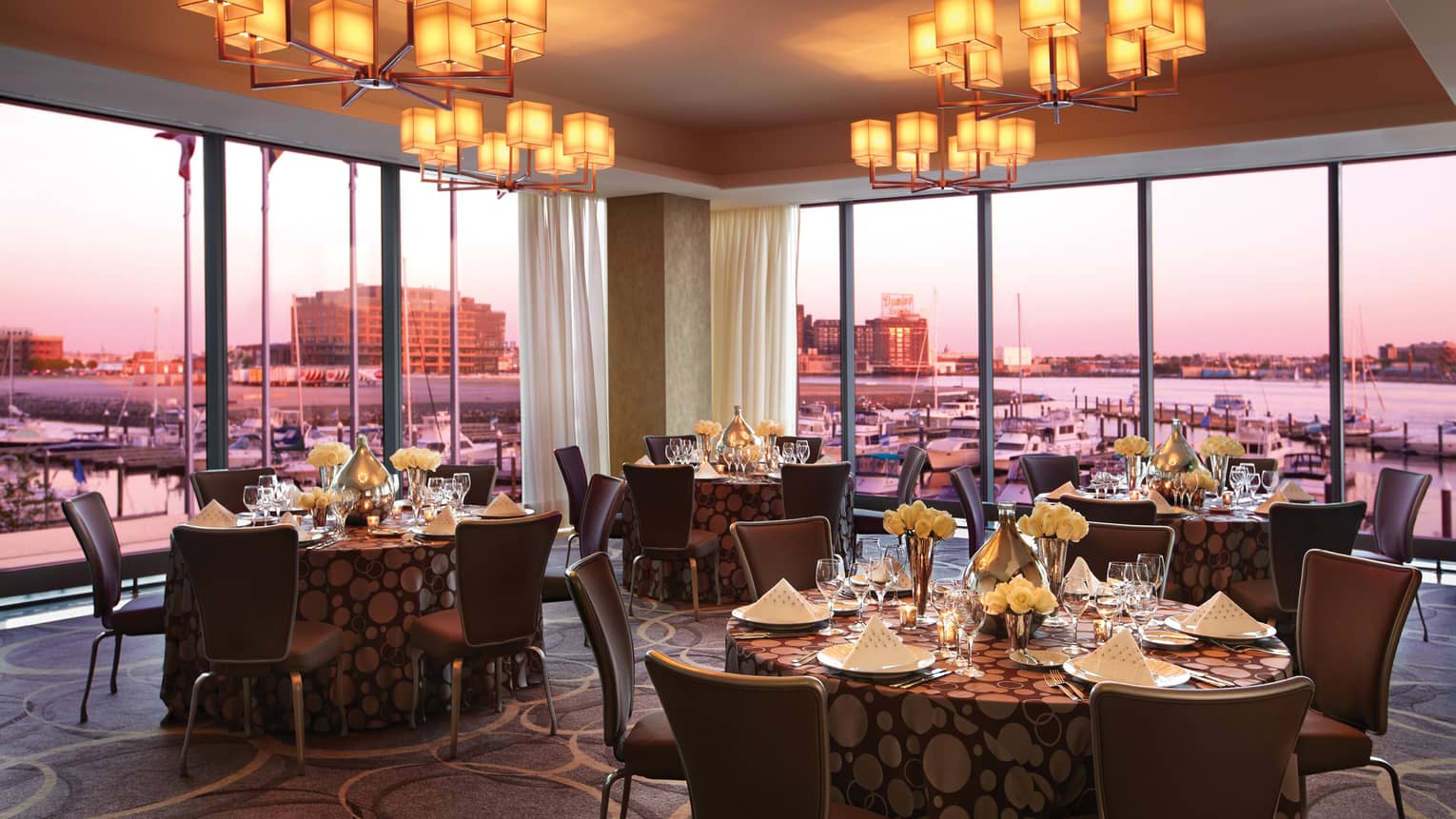 Cerulean banquet room dining tables by corner floor-to-ceiling windows, sunset views
