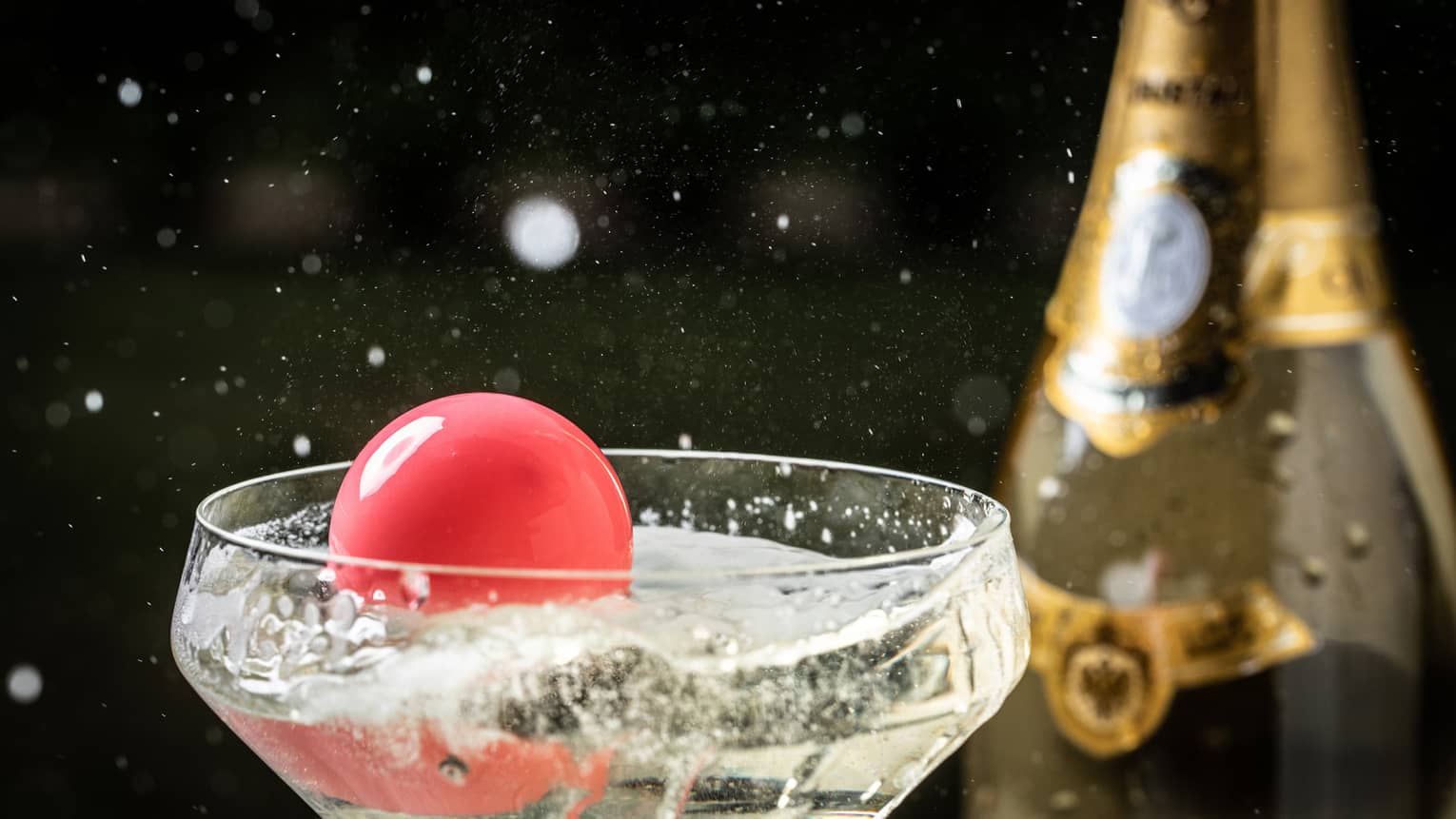 A close up of a pink ball floating in a glass of champagne