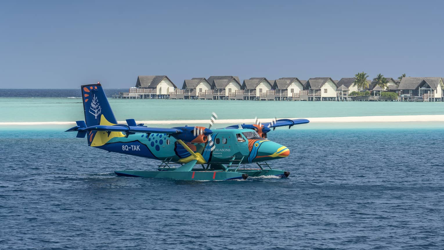 The Four Seasons sea plane landing on calm water in front of beach houses and palm trees