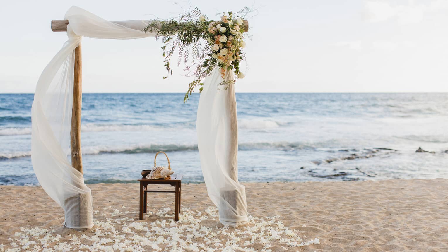 Sand beach wedding altar with flowers, white linens flowing in breeze