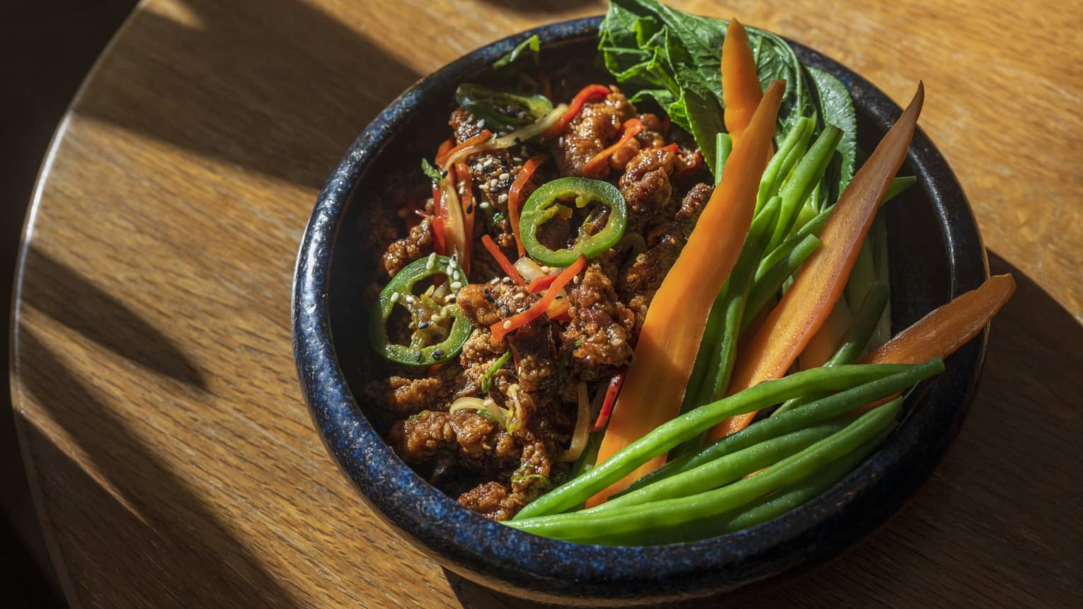 Spicy crispy beef served in a black bowl with green beans, carrots, green onion, ginger and jalape�os