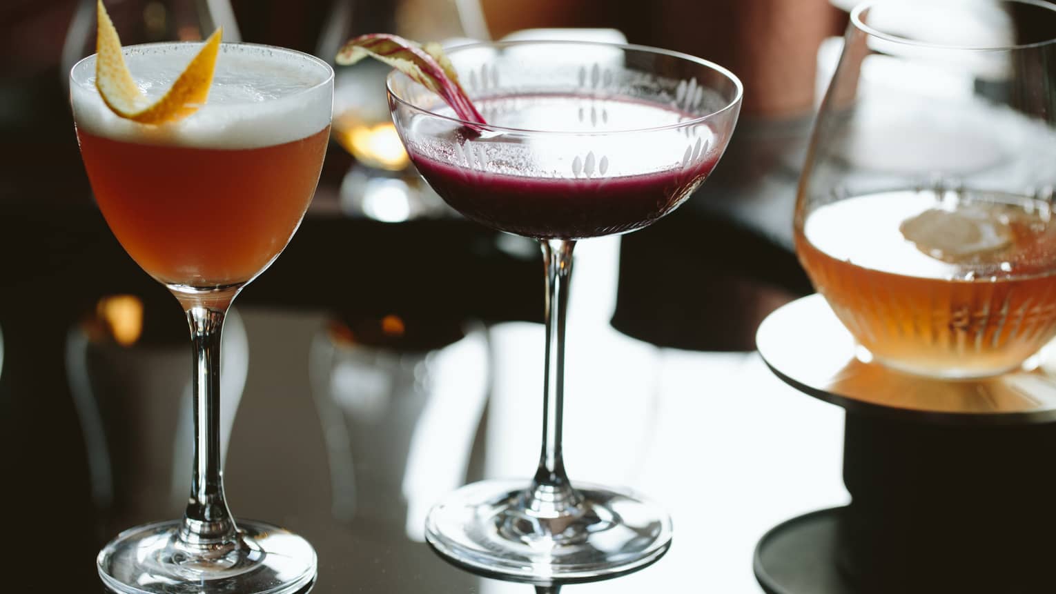 Three gourmet fall cocktails in glasses with rind garnishes 