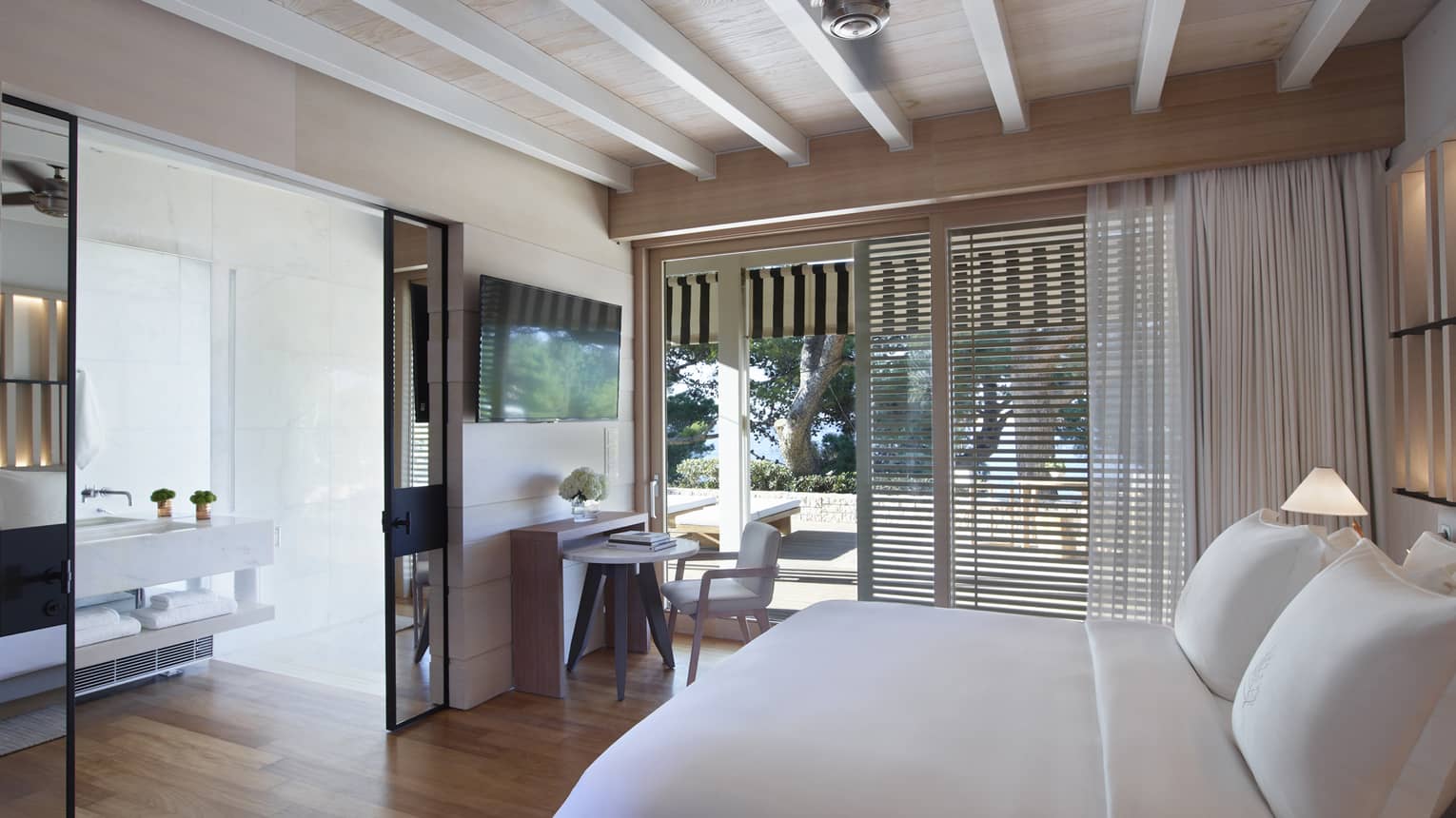 Guest room with white king bed, exposed rafter ceiling, sliding doors opening onto patio, mirrored doors to bathroom