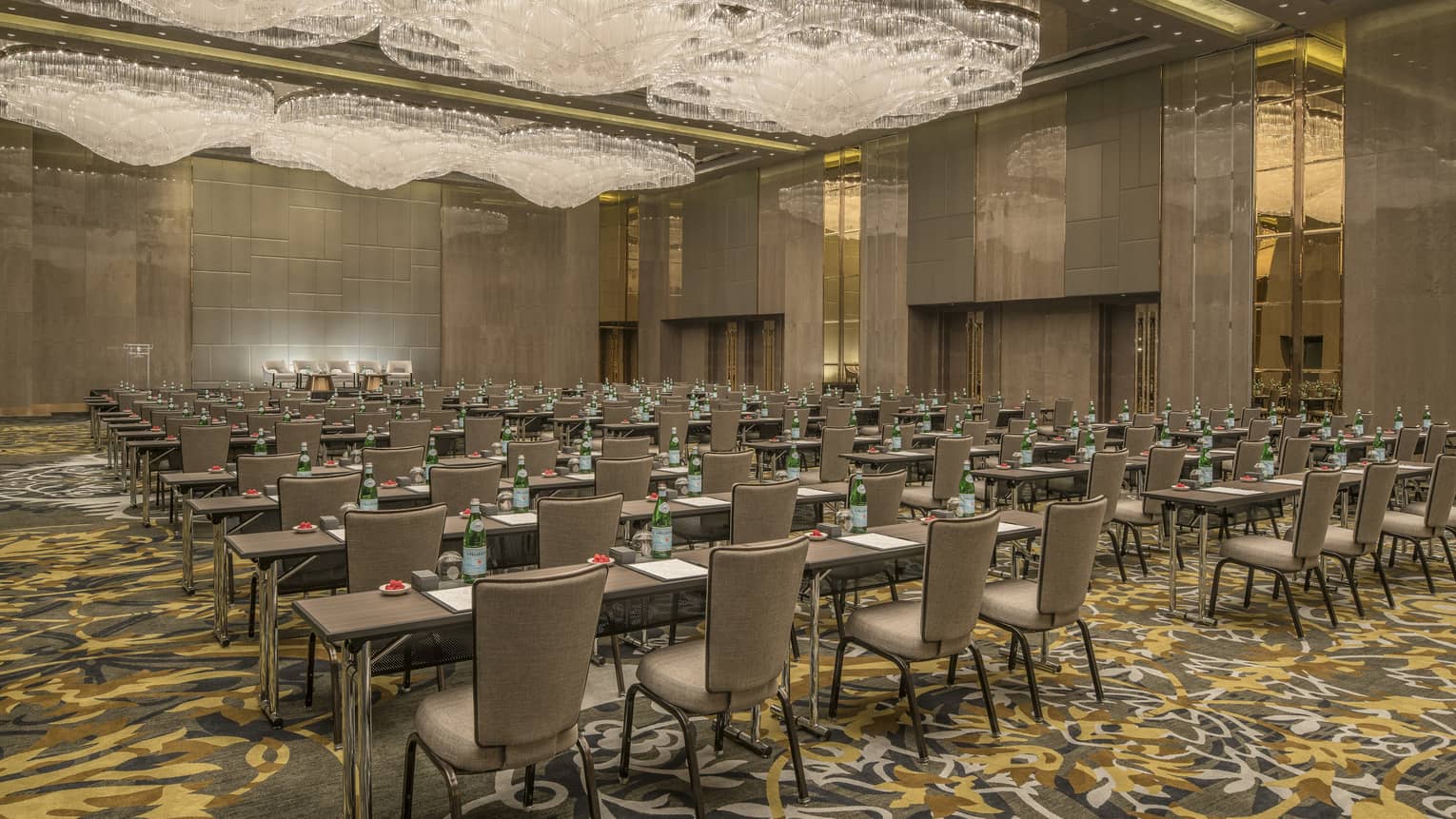 Rows of meeting tables, chairs under large crystal chandeliers in carpeted ballroom