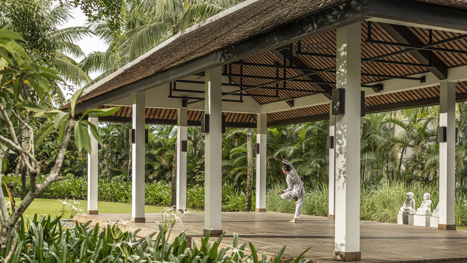 Man practices yoga at an outdoor yoga pavilion surrounded by palm trees