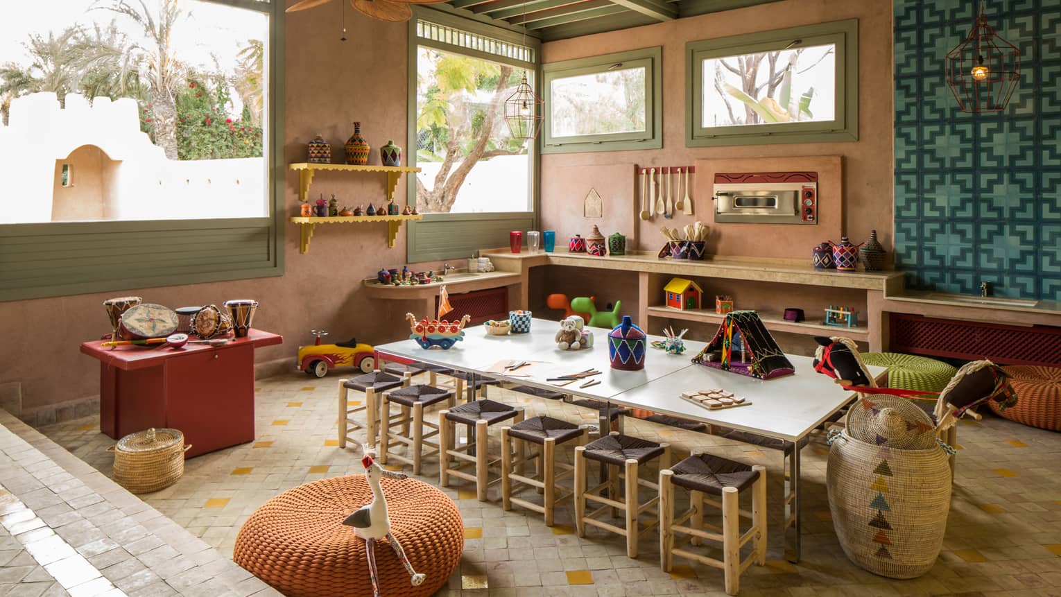 Kids Club long craft table with stools, toys on shelves along wall under sunny windows