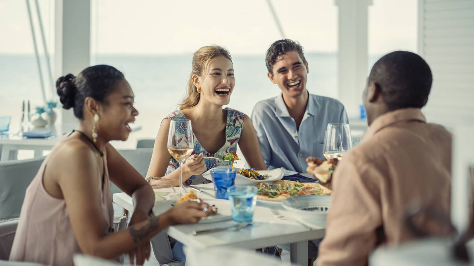 Two couples laugh as they share a meal at Blu Beach Club