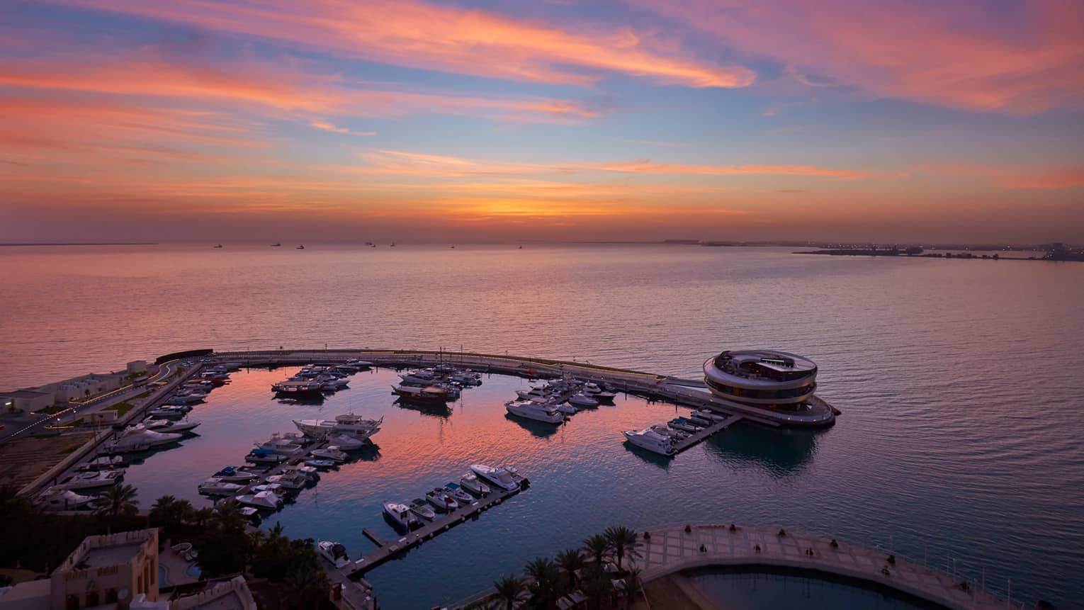Aerial view of private Four Seasons Marina against the gulf, pink sky at sunset 