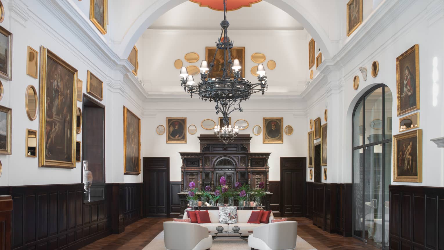 Sala Museo with artwork lining both walls, white leather furniture, high ceilings, wrought iron chandelier, fireplace